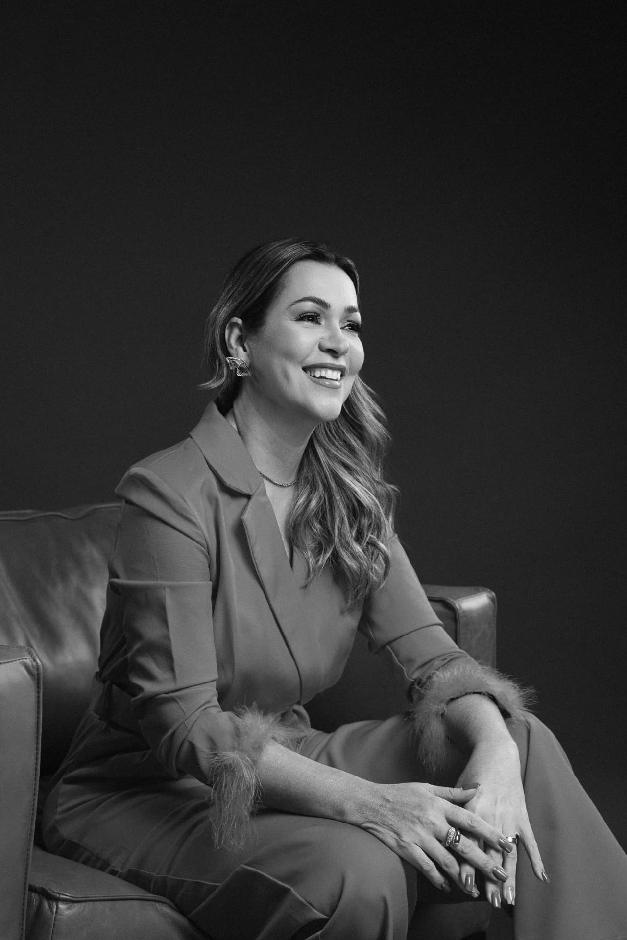Thatiane Cardoso sentada em uma poltrona, sorrindo